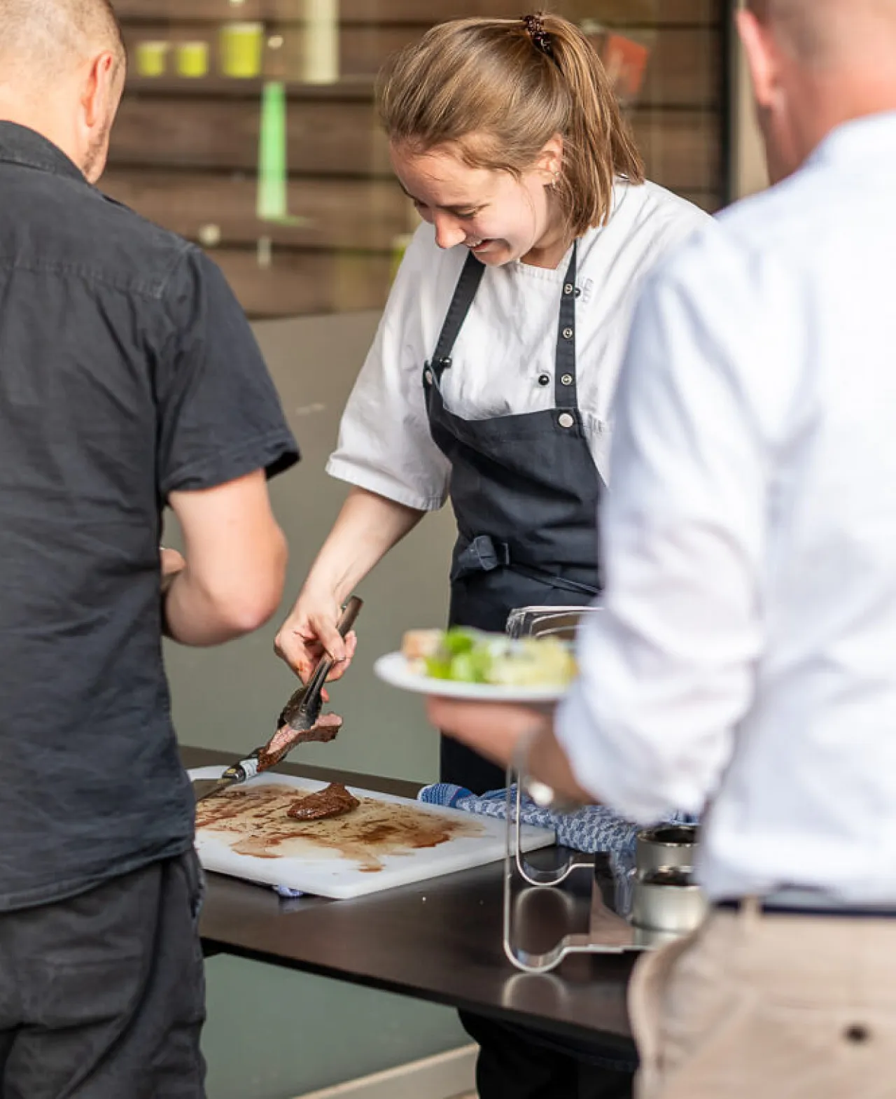 Junge, fröhliche Kellnerin wendet und serviert Grillfleisch auf einem Brettchen